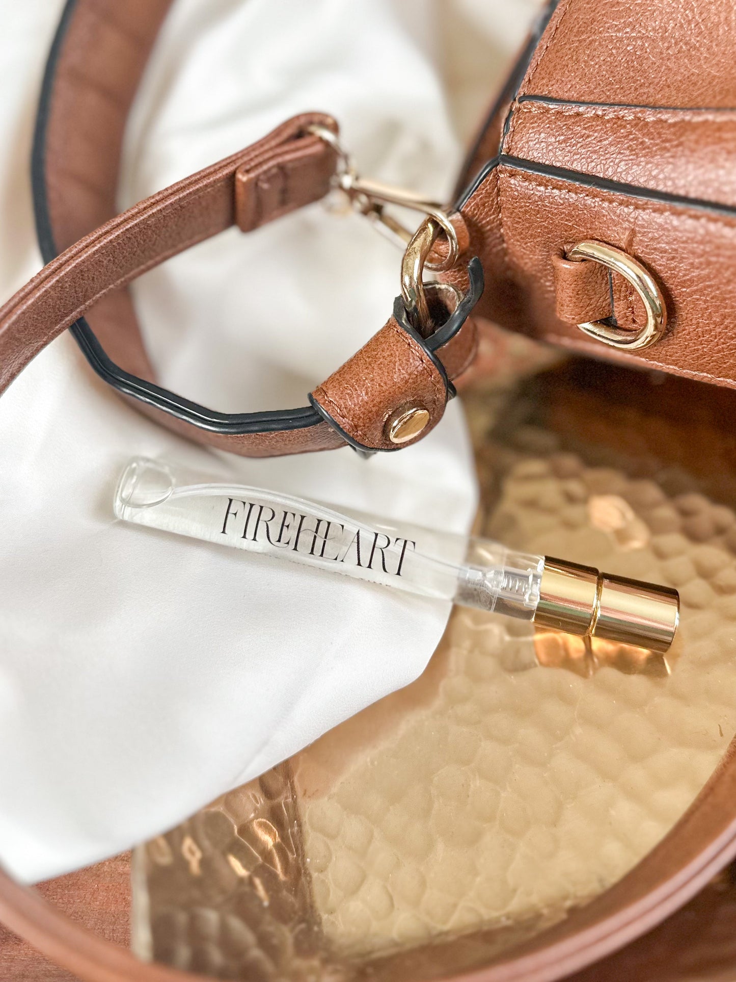 Perfume bottle labeled 'Fireheart' on a reflective surface with a brown leather bag in the background.
