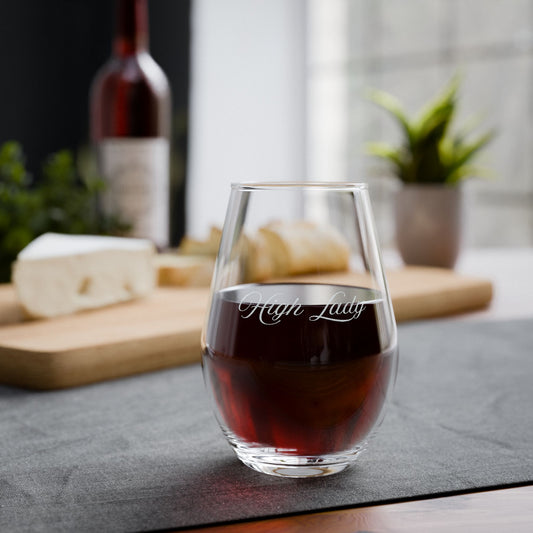 Stemless wine glass engraved with "High Lady" with red wine on a table with cheese and bread.