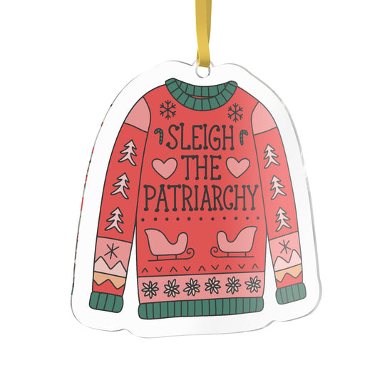 A novelty Christmas ornament shaped like a sweater, featuring the text 'SLEIGH THE PATRIARCHY' in black lettering on a red and pink patterned design with green ribbed trim, hanging from a yellow ribbon.