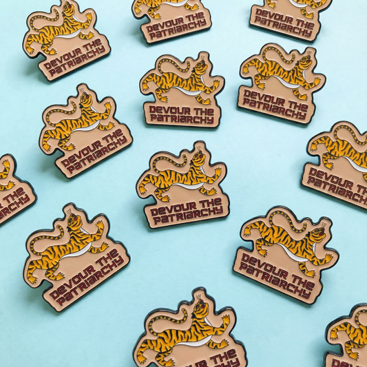 Tiger-themed pins with 'Devour the Patriarchy' text on a blue background