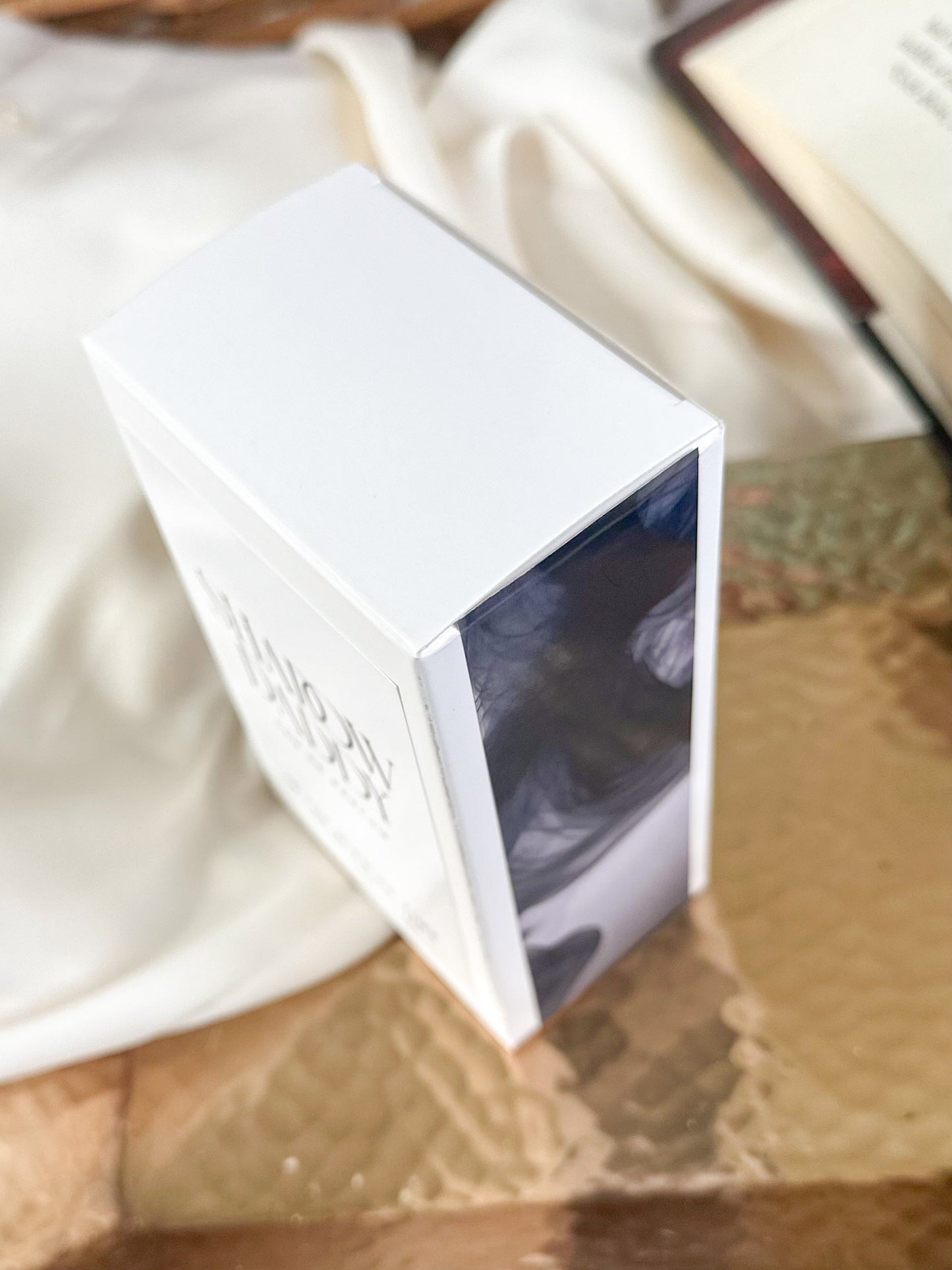 White rectangular perfume box with a textured surface on a reflective copper surface