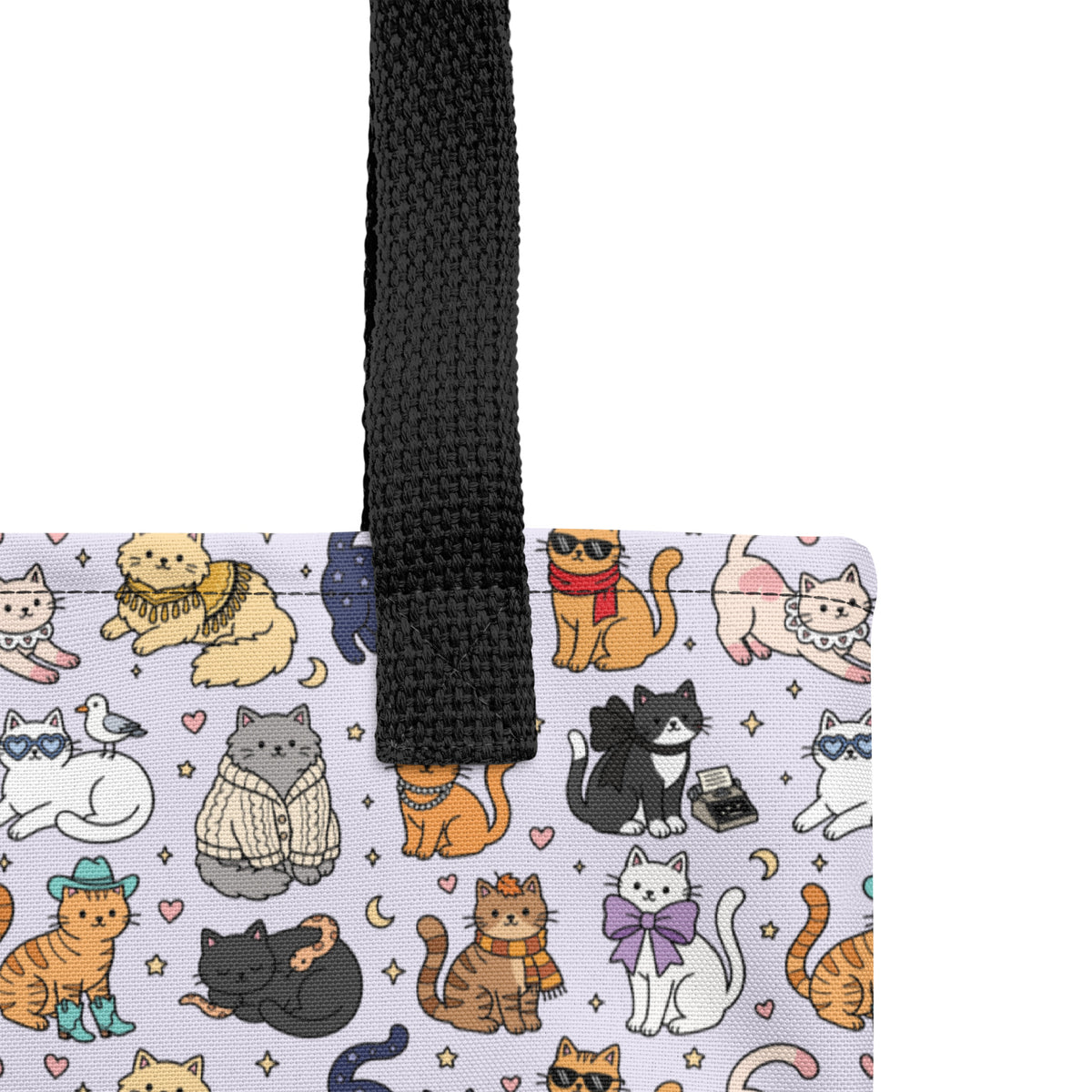 A close-up of a tote bag corner showing a white fabric body printed with a colorful cartoon cat pattern and a black woven handle, photographed against a white background.