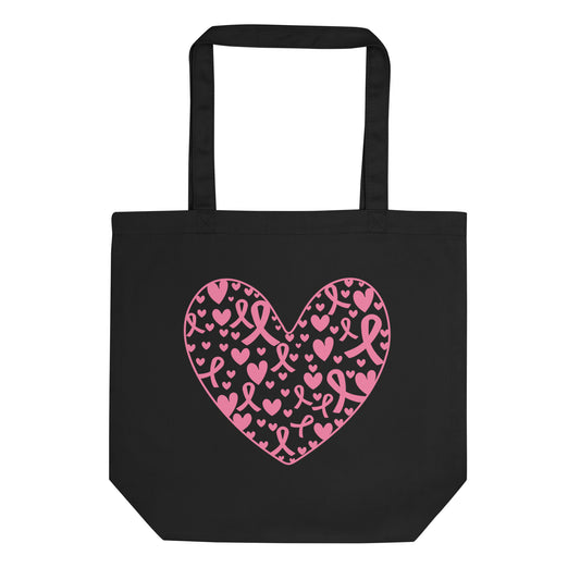 A black canvas tote bag with two black shoulder straps, featuring a large pink heart graphic on the front filled with smaller pink hearts and ribbon motifs for breast cancer awareness, shown against a plain white background.