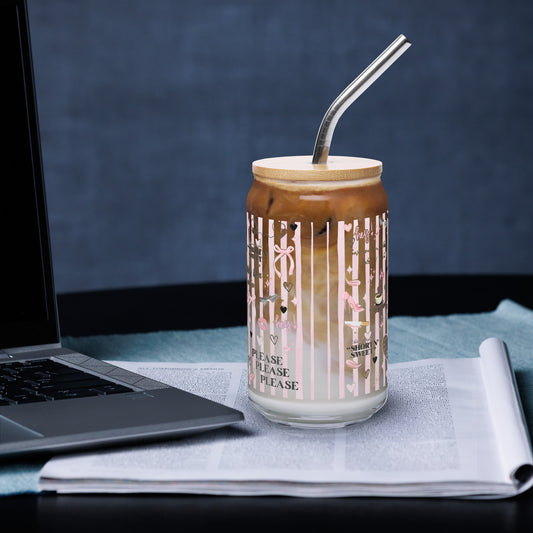 Coquette glass tumbler with a bamboo lid and straw on a desk beside a laptop, decorated with pink stripes, hearts and espresso art, filled with iced coffee and cream.