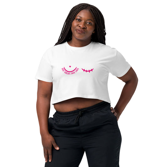 Woman wearing a white t-shirt with a pink breast cancer awareness graphic featuring a pair of half circles, one with a heart above it and text 'self-checks save lives' the other with mastectomy stiches, and black pants on a white background