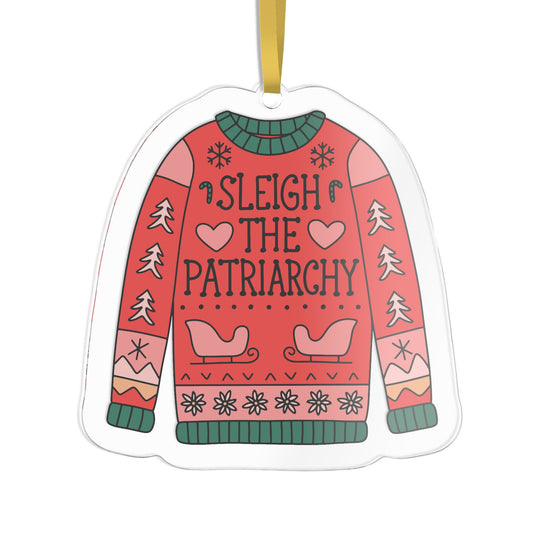 A novelty Christmas ornament shaped like a sweater, featuring the text 'SLEIGH THE PATRIARCHY' in black lettering on a coral-red background with green and pink holiday patterns, hanging from a gold ribbon.