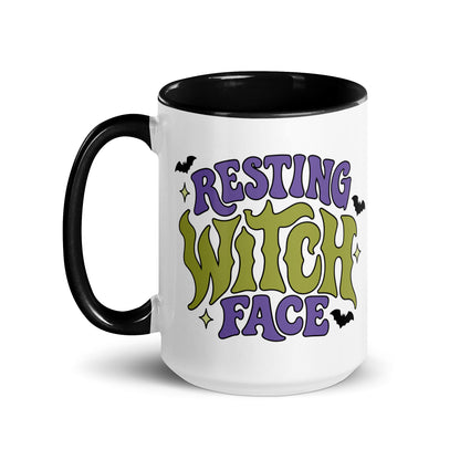 A white ceramic mug with a black handle and black interior, featuring the text 'RESTING WITCH FACE' in purple and green gothic lettering with small black bats and yellow stars.