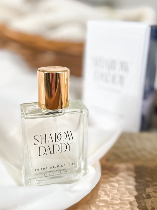 Perfume bottle labeled 'Shadow Daddy' on a reflective surface with a blurred background
