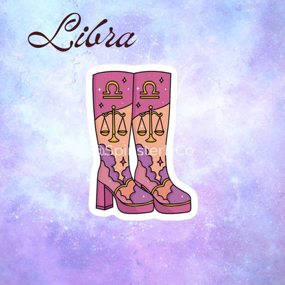 A die-cut sticker featuring an illustration of pink and purple high-heeled boots with gold Libra zodiac symbols, shown against a pastel purple and blue galaxy background with the word 'Libra' written at the top.