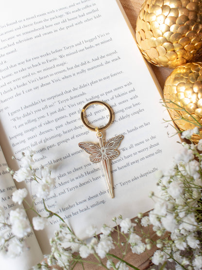Faerie Dagger Enamel Keychain by Meaggie Moos with gold metal accents, hard enamel dagger on a book
