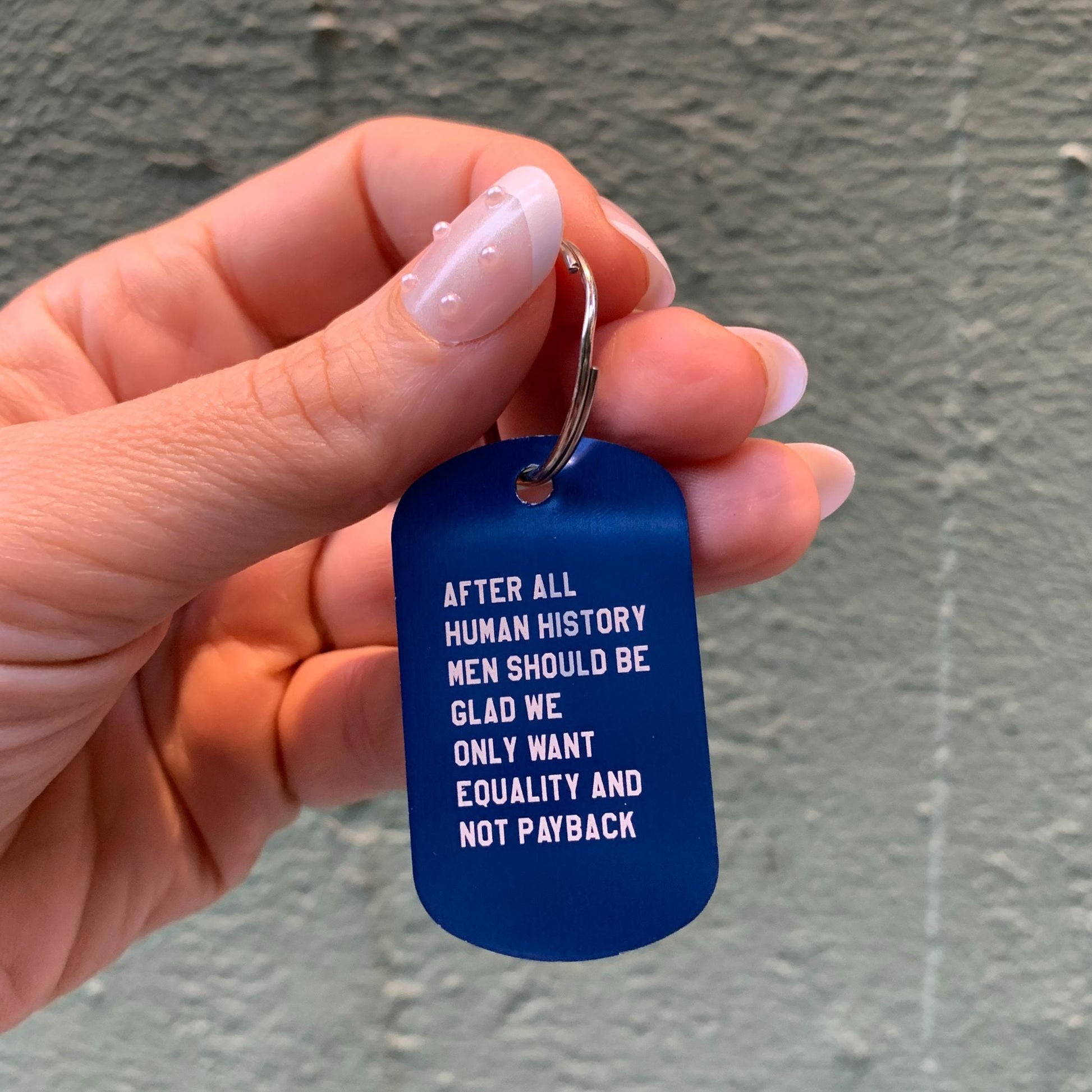 Hand holding a blue keychain with white text against a gray background