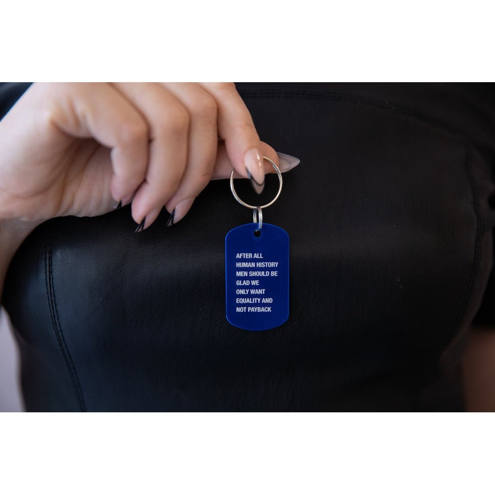 Hand holding a blue keychain with text against a black background