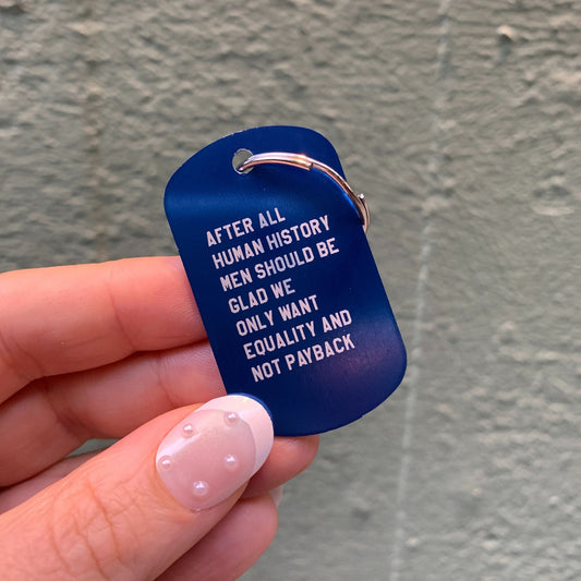 Blue keychain with text held by a hand against a gray background