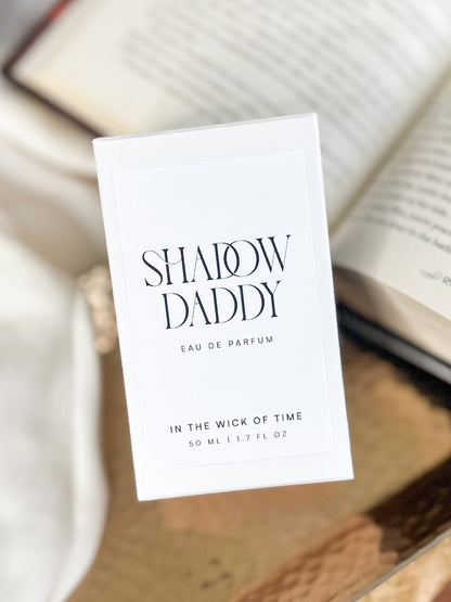 Perfume label for 'Shadow Daddy' on a textured surface with an open book blurred in the background