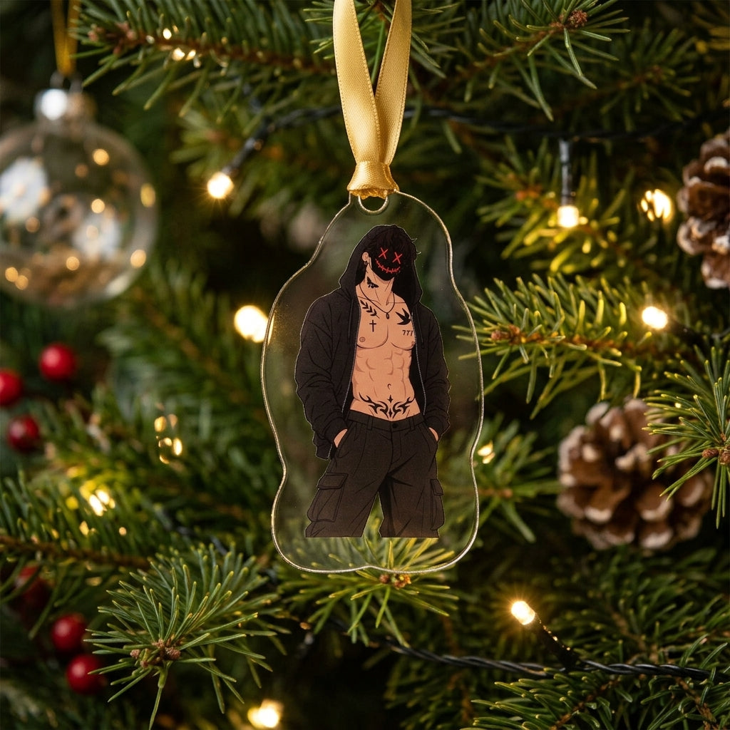 An acrylic Christmas ornament shaped like a character hanging from a gold ribbon on a decorated Christmas tree with pine branches, warm string lights, and ornaments.