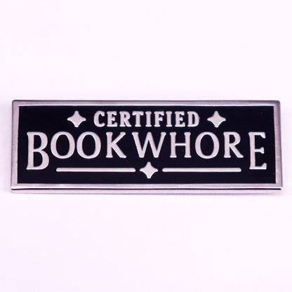 Enamel pin with 'Certified Bookwhore' text on a black background