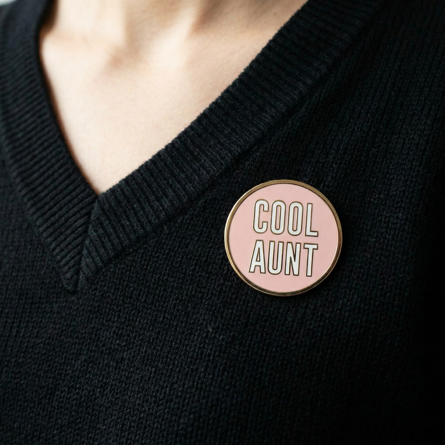 Person wearing a black sweater with a 'Cool Aunt' pin on a pink background