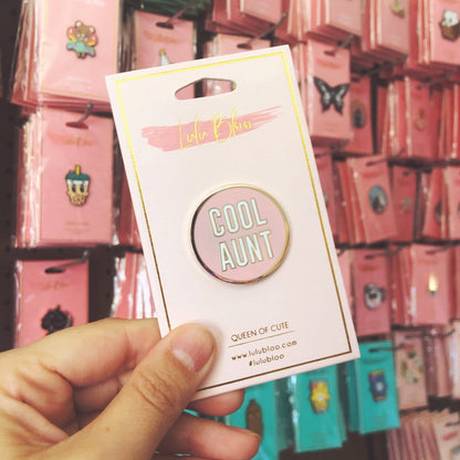 Pin with 'Cool Aunt' text on a card held in front of a display of similar products.