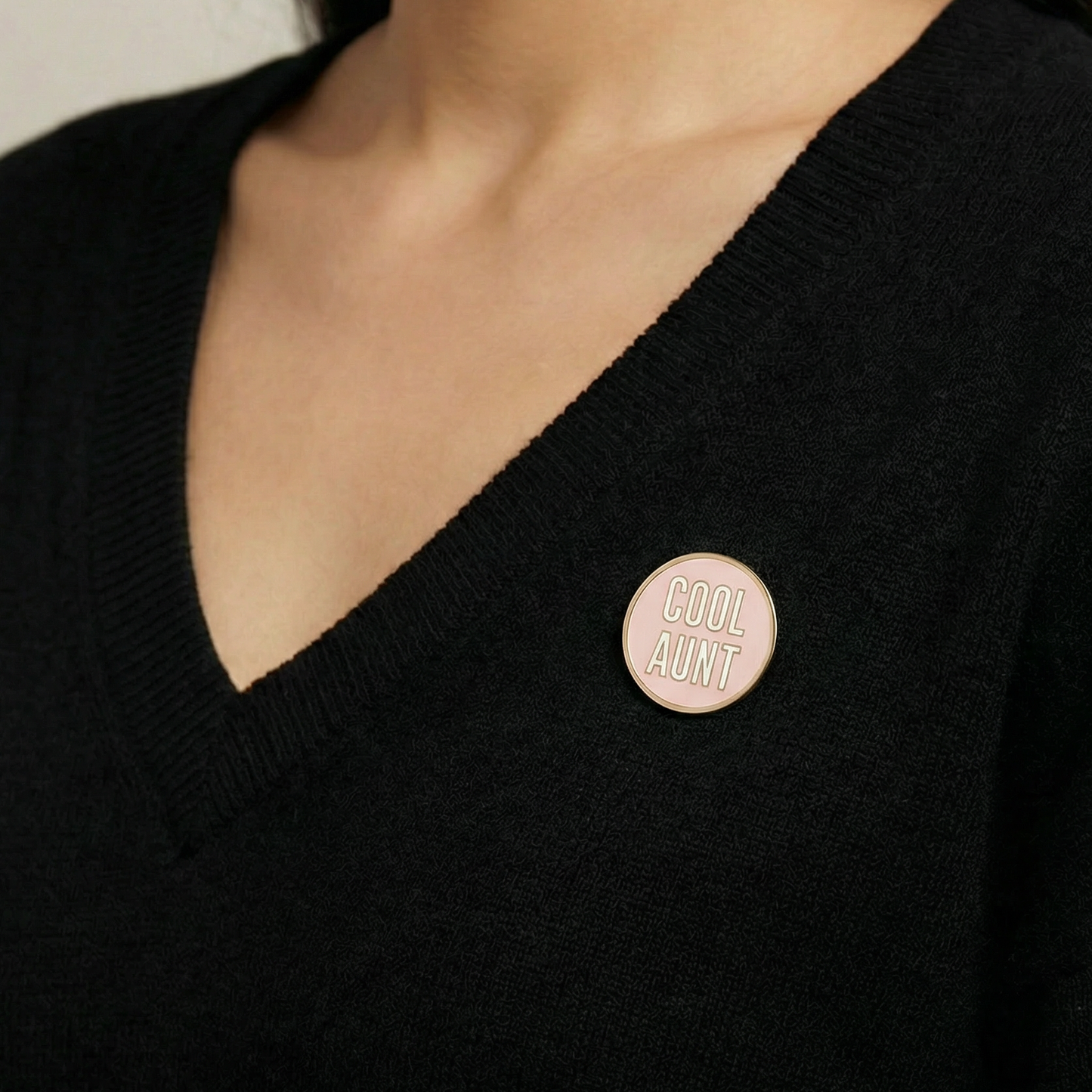 Person wearing a black sweater with a 'Cool Aunt' pin on a neutral background