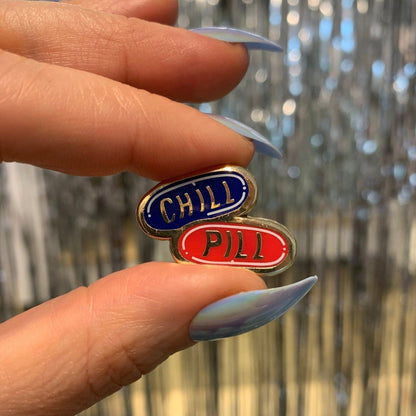 Hand holding two small metal signs labeled 'Chili Pill' against a blurred background