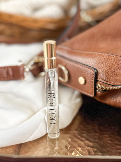 Perfume bottle labeled 'High Lord' on a reflective surface with a brown leather bag in the background.