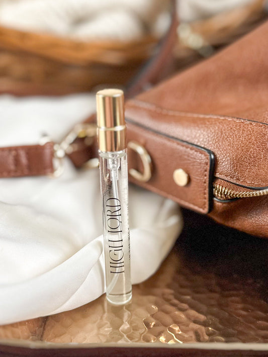 Perfume bottle labeled 'High Lord' on a reflective surface with a brown leather bag in the background.