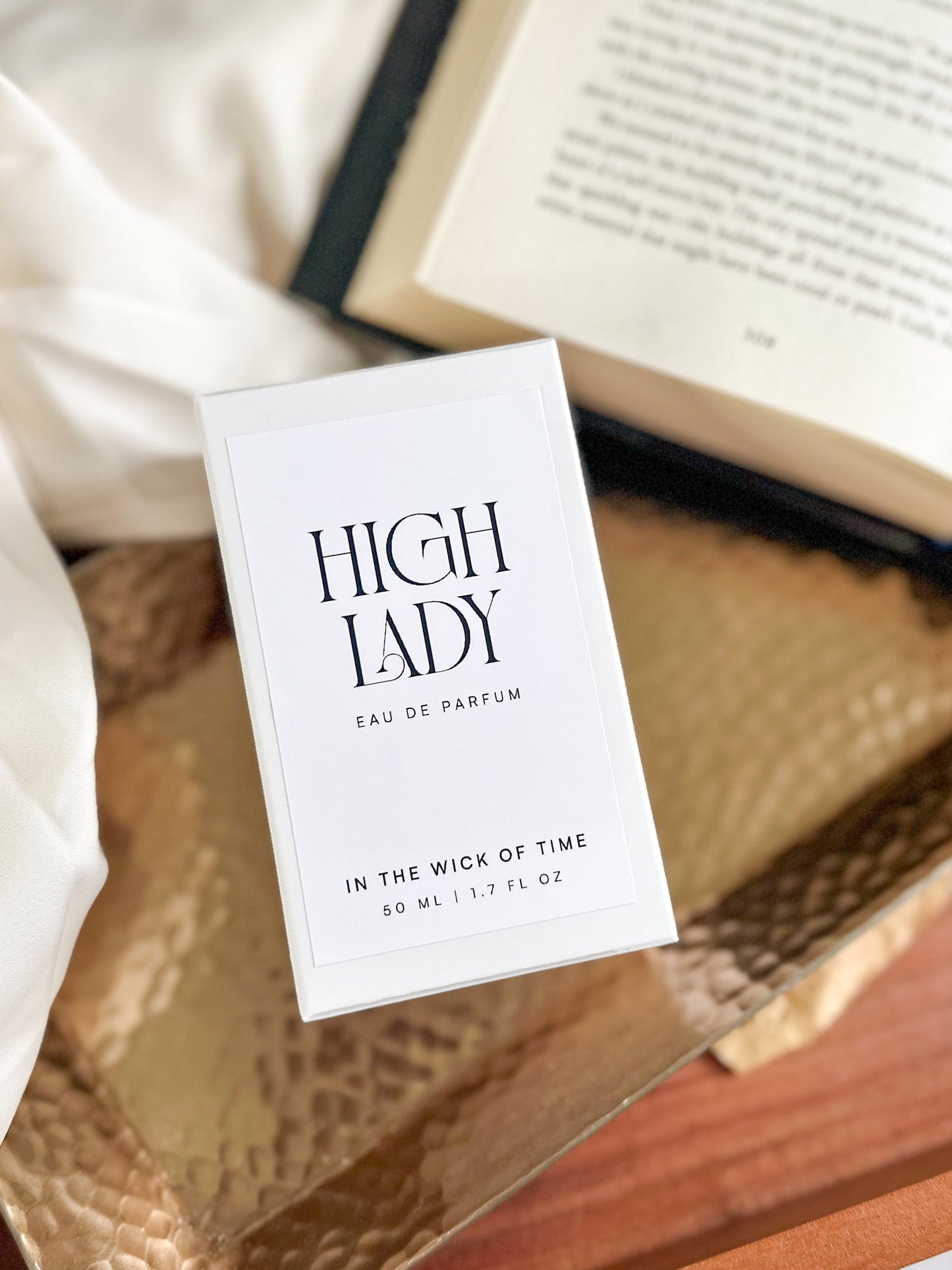 Perfume packaging labeled 'High Lady' on a textured surface with a book in the background.