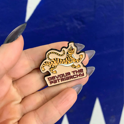 Hand holding a pin with a tiger design and text against a blue background