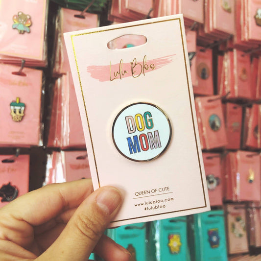 Pin with 'DOG MOM' text on a Lulu & Boo branded card, held against a display of similar products.