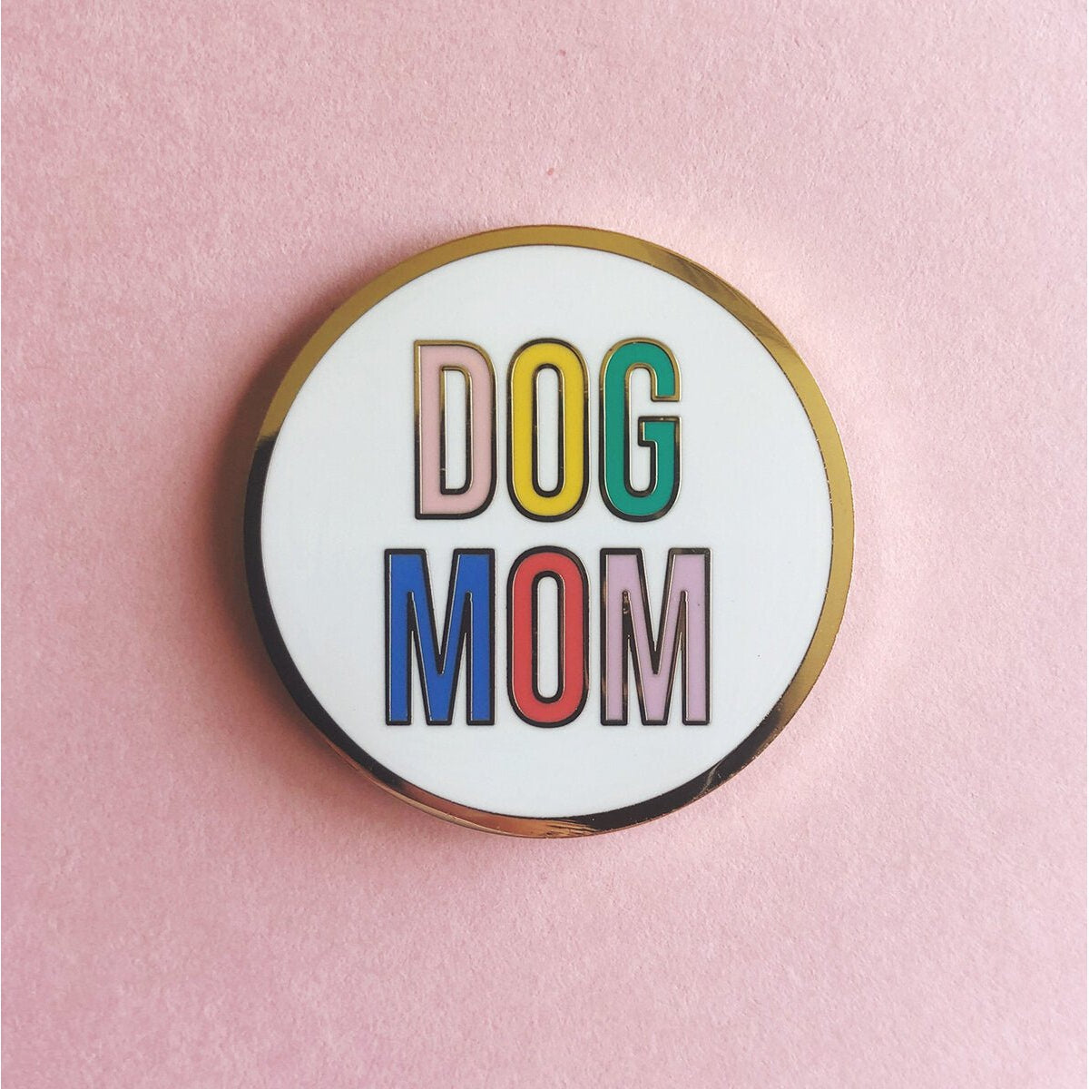 Round enamel pin with 'DOG MOM' text in colorful letters on a pink background