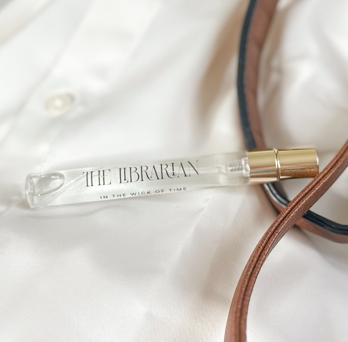 Small glass bottle with gold cap labeled 'The Librarian' on a white fabric background