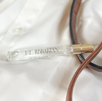 Small glass bottle with gold cap labeled 'The Librarian' on a white fabric background