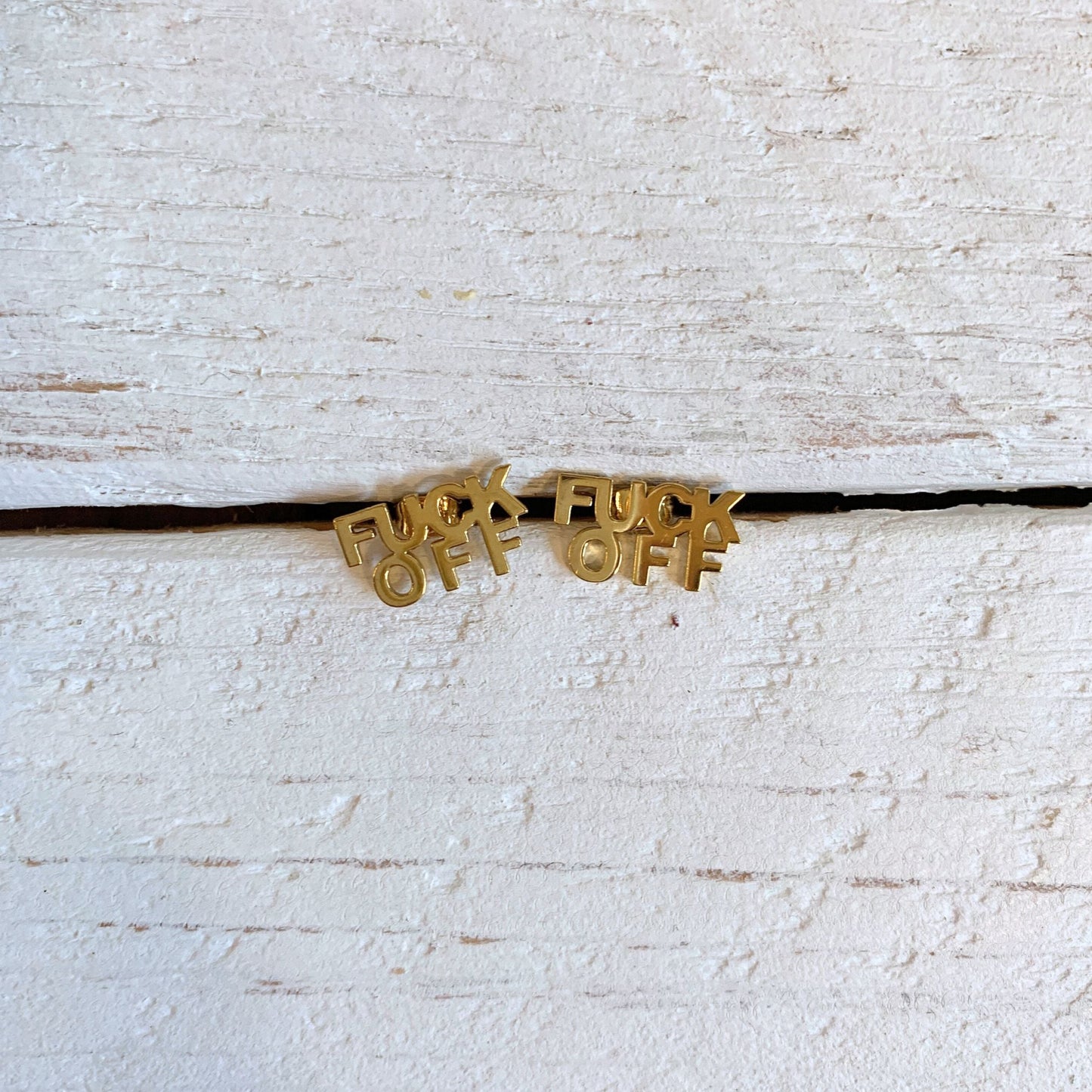 Gold necklace with 'F**K OFF' pendants on a textured white surface
