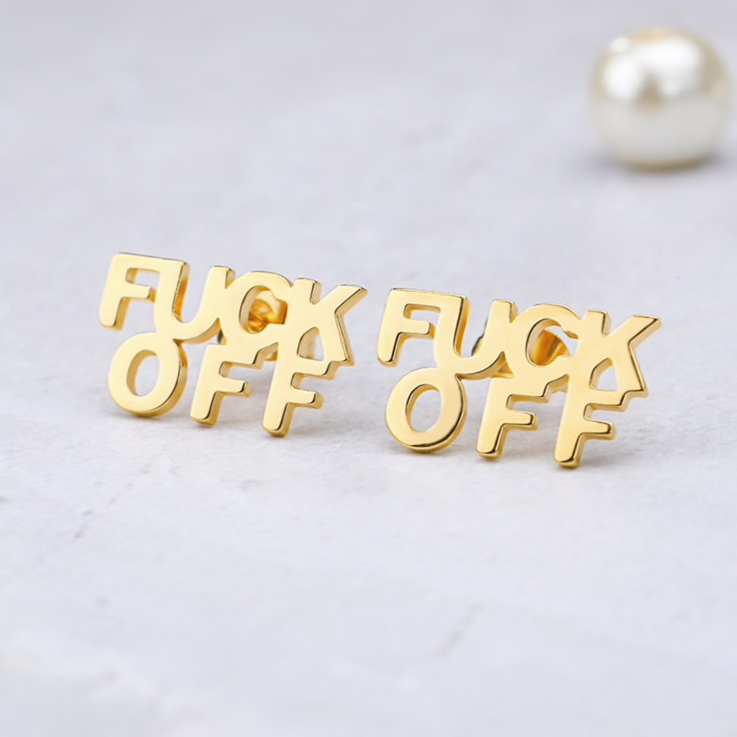Gold 'F*CK OFF' earrings on a light gray background