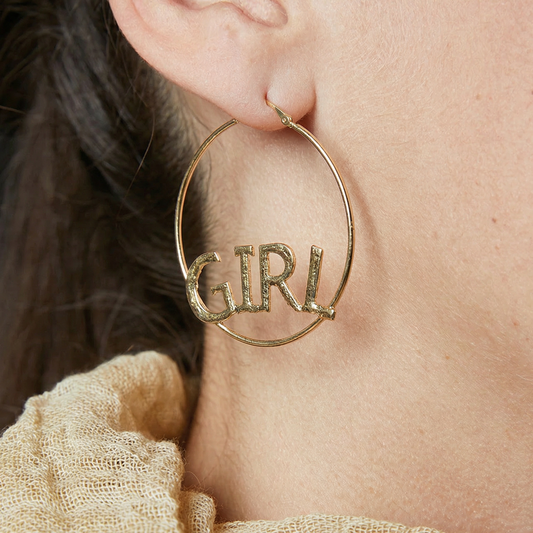 Gold hoop earring with 'GIRL' text worn by a person