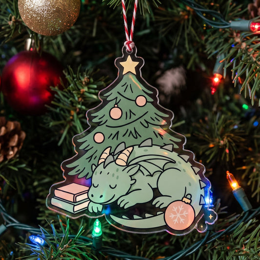 A die-cut Christmas ornament shaped like a sleeping dragon under a Christmas tree, hanging on a decorated Christmas tree with colorful lights and ornaments.