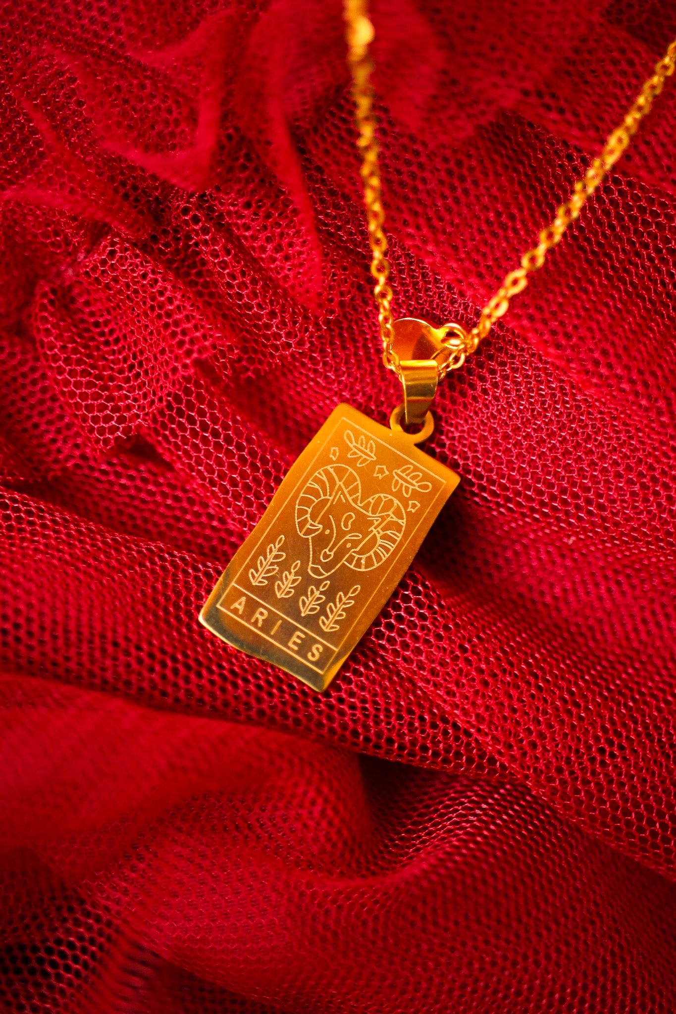 Gold pendant with 'Aries' text on a red fabric background