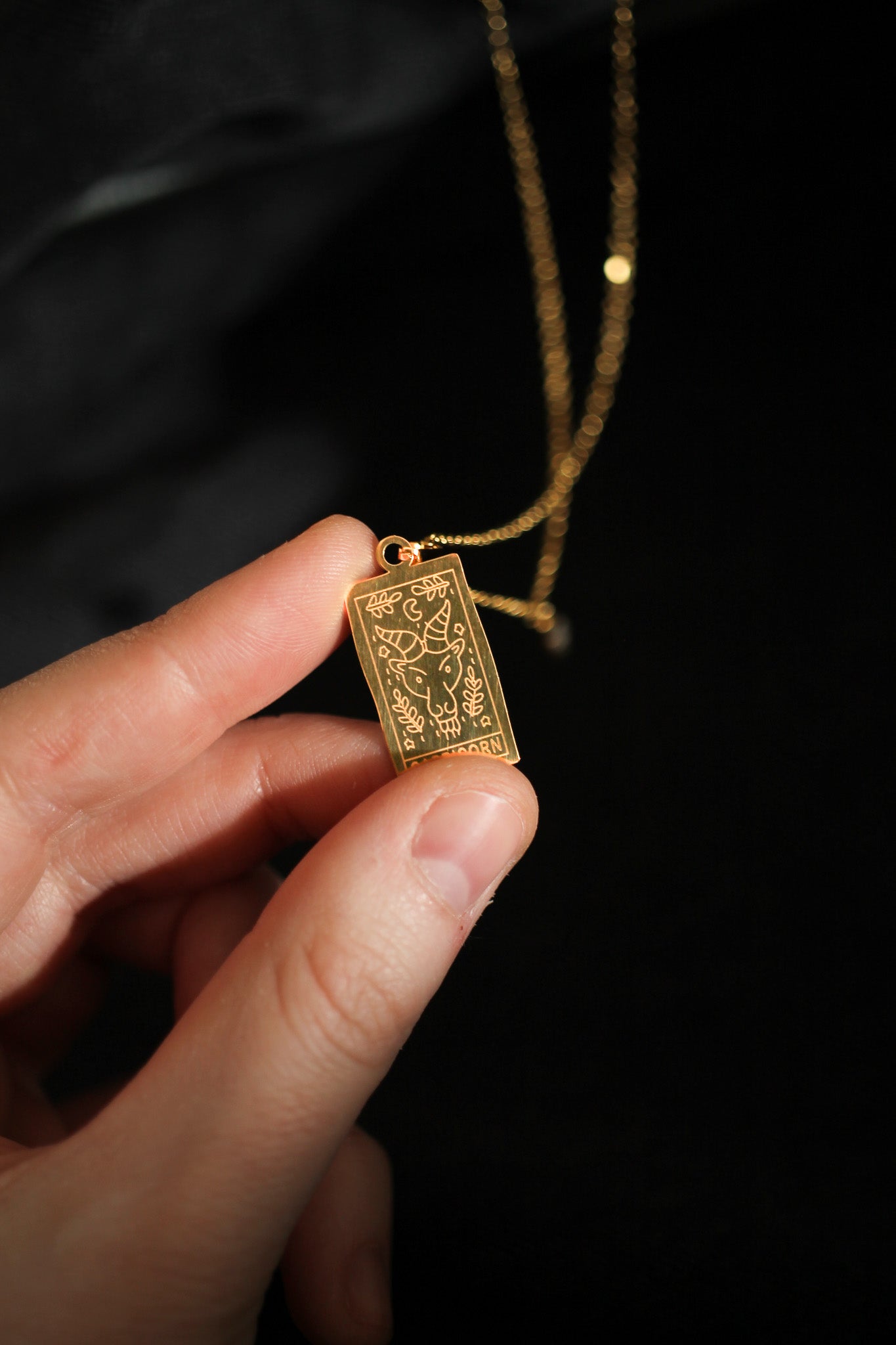 Gold pendant held by a hand against a dark background