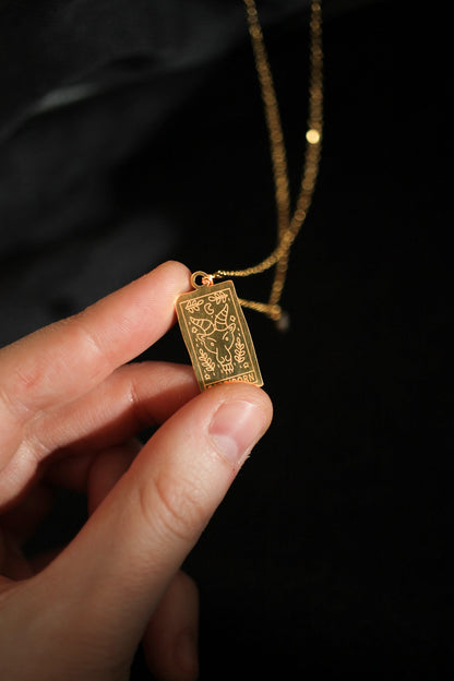 Gold pendant held by a hand against a dark background
