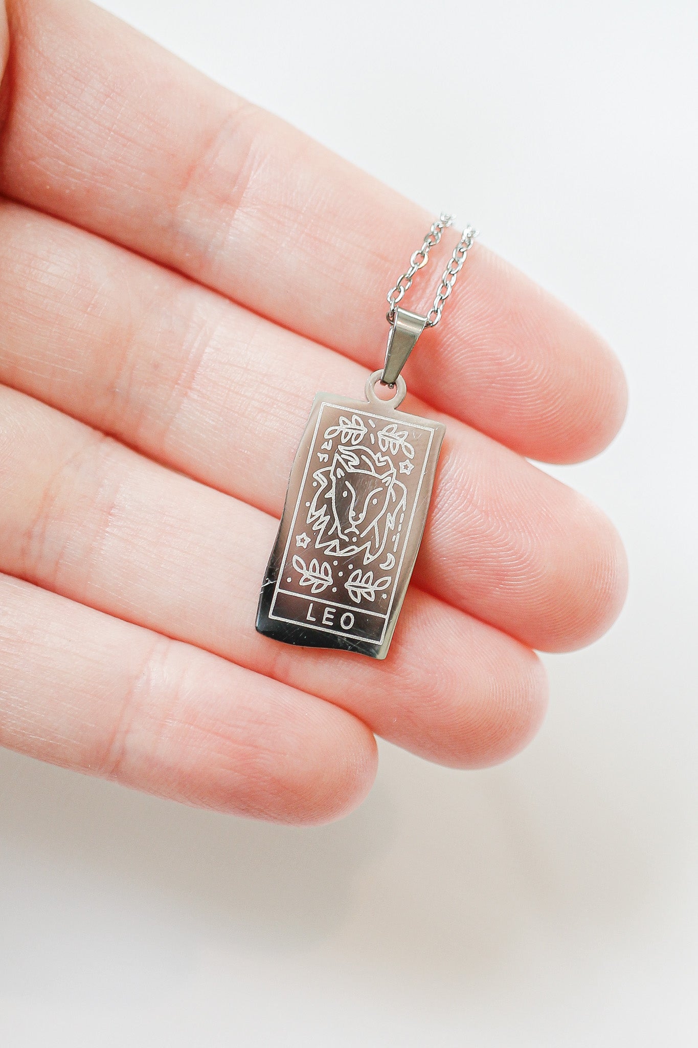 Silver pendant with 'Leo' symbol held between fingers on a white background