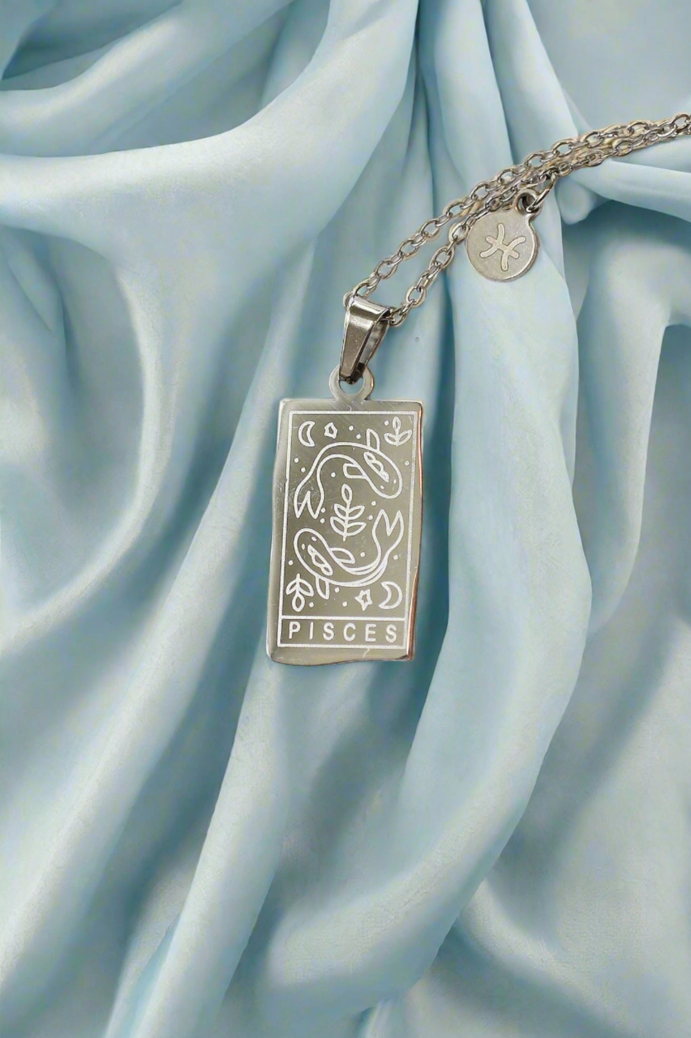 Silver Pisces zodiac pendant necklace on a light blue satin background