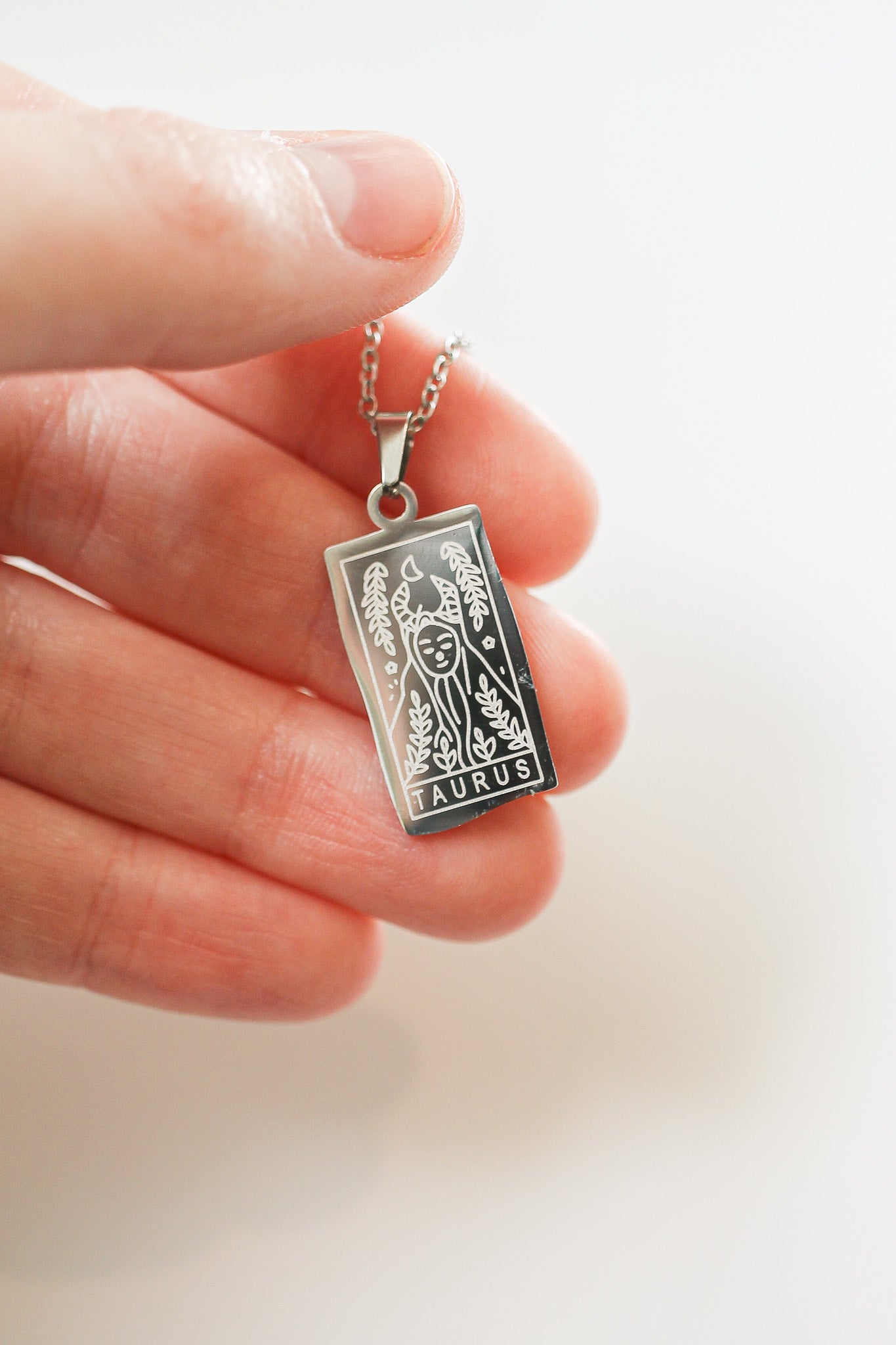 Silver Taurus zodiac pendant held between fingers on a light background