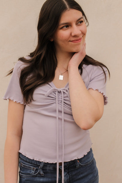 Woman wearing a light purple top with lace sleeves against a beige background