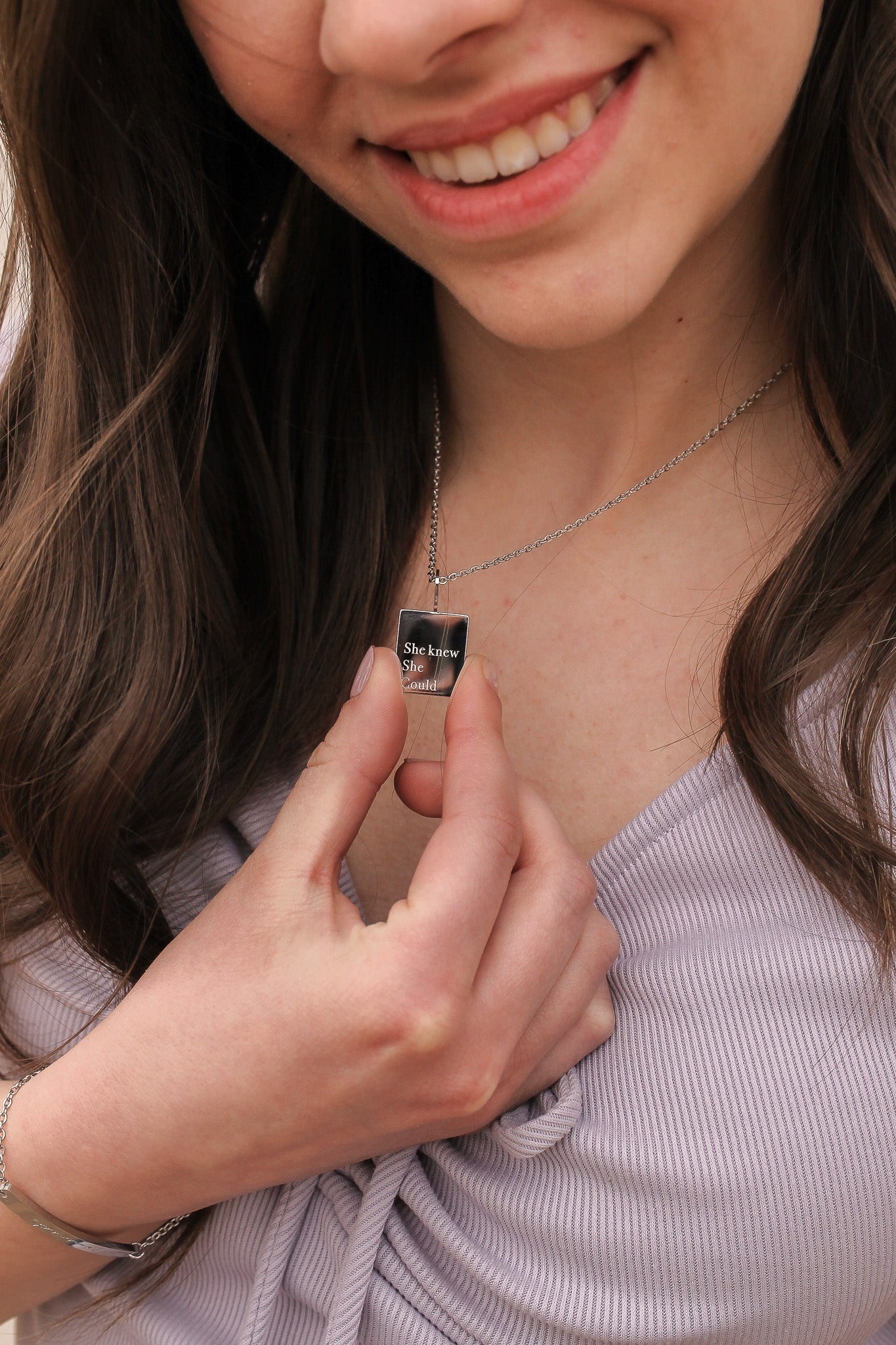 Person holding a small rectangular object with a design on it, wearing a necklace.