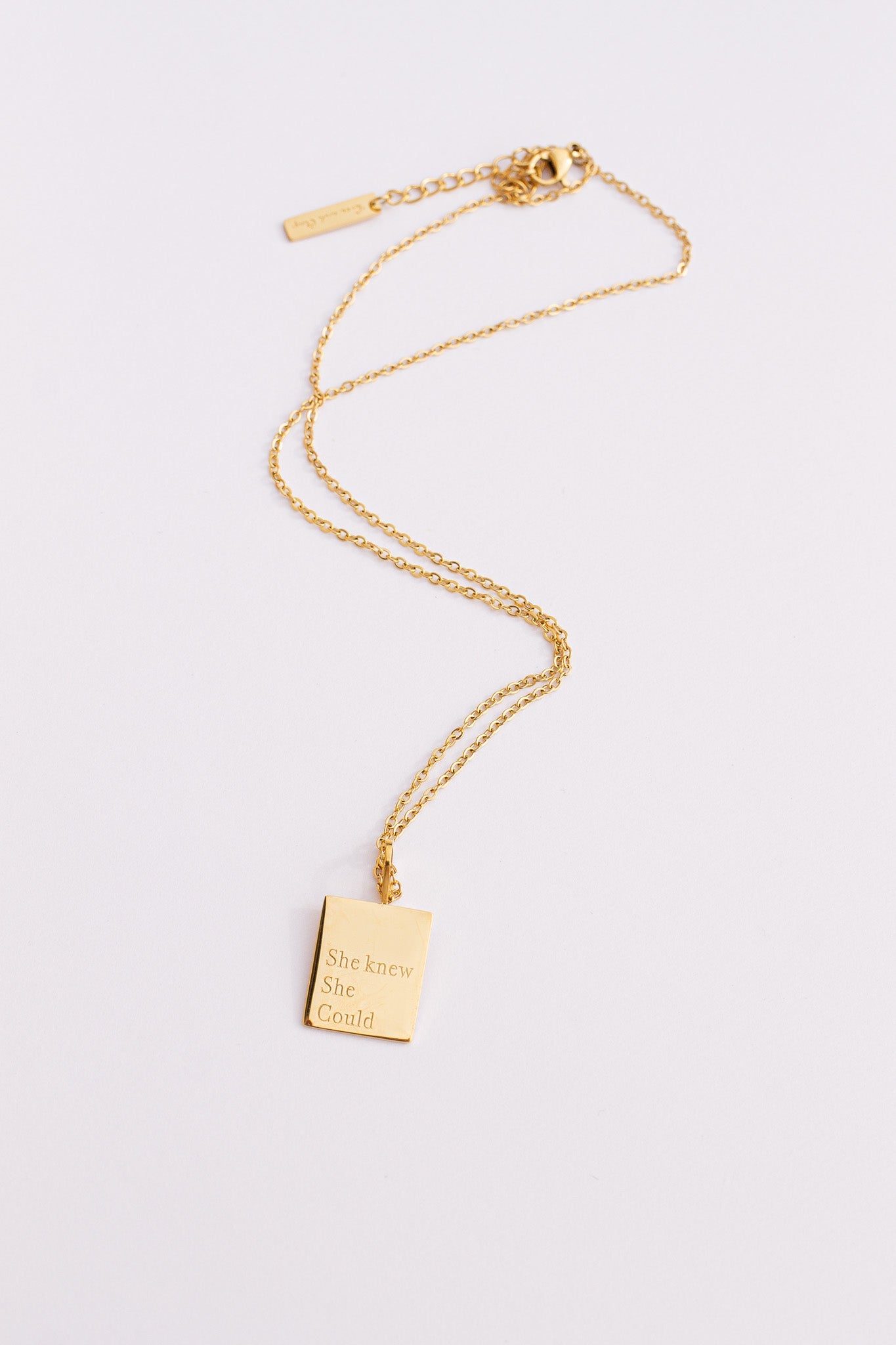 Gold necklace with a rectangular pendant on a light gray background