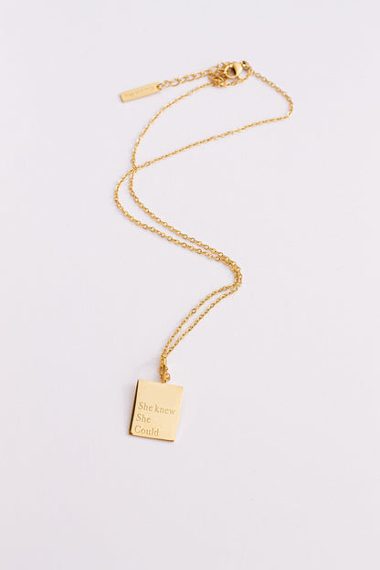 Gold necklace with a rectangular pendant on a light gray background