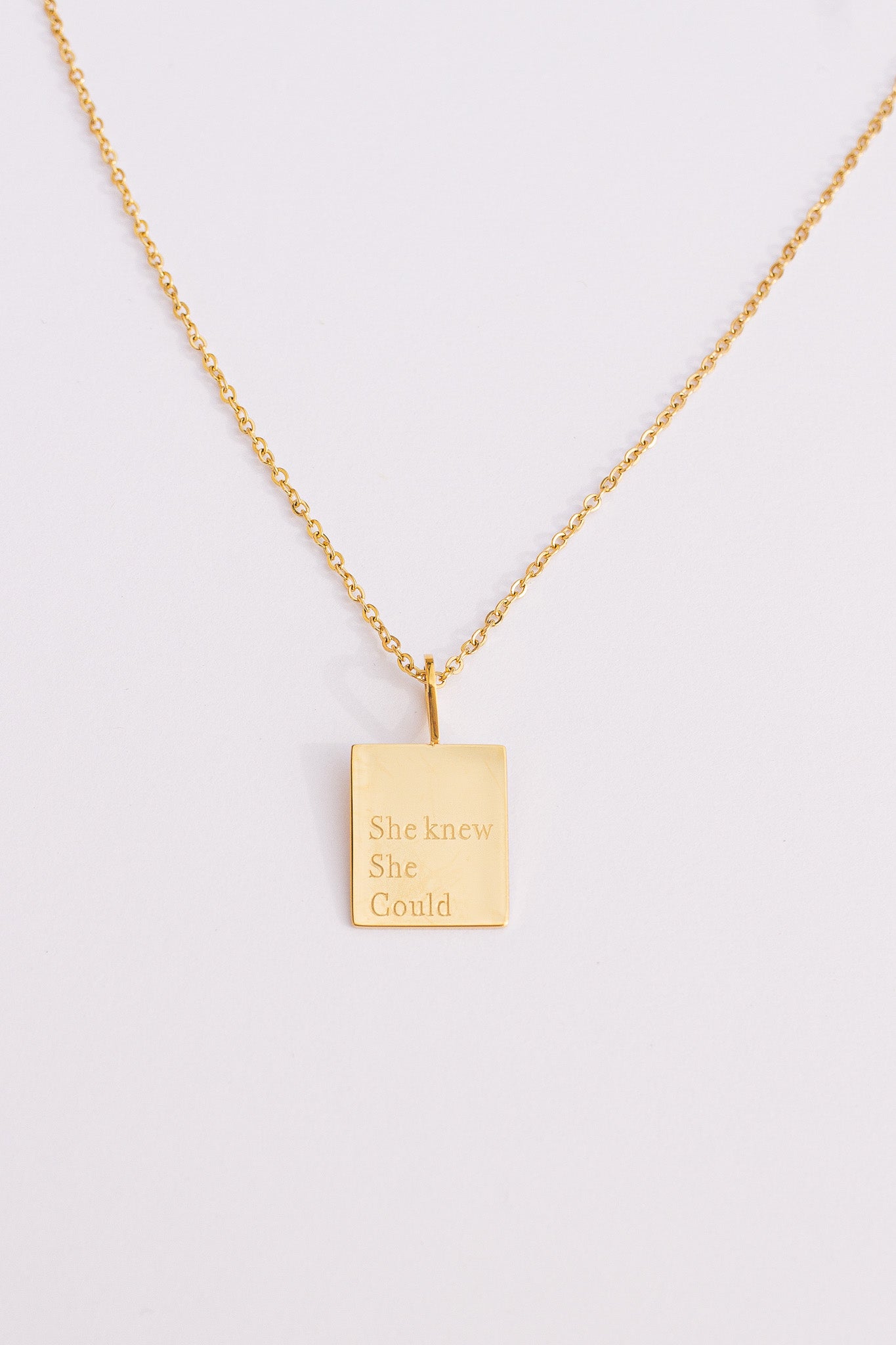 Gold necklace with a rectangular pendant on a light gray background