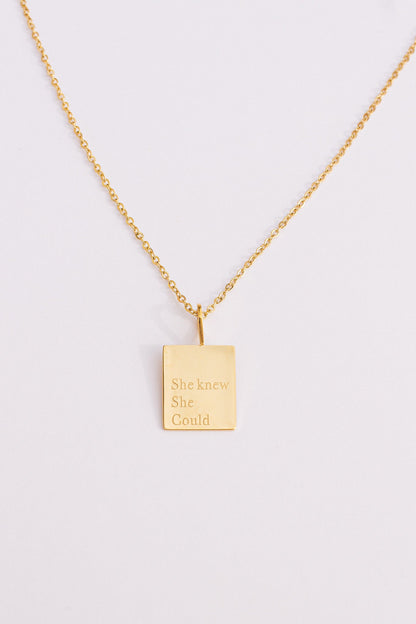 Gold necklace with a rectangular pendant on a light gray background