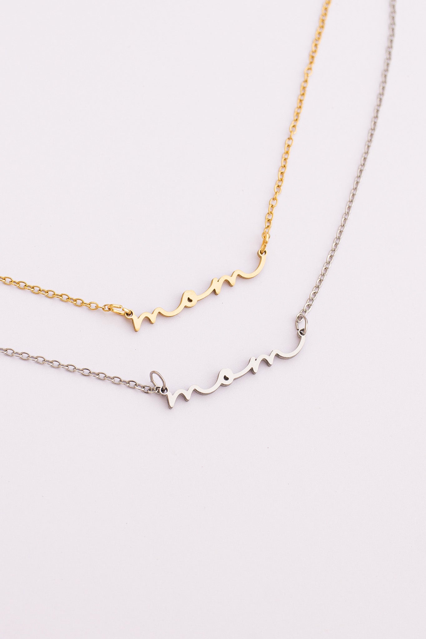 Two gold necklaces with 'mom' and 'mommy' inscriptions on a light pink background