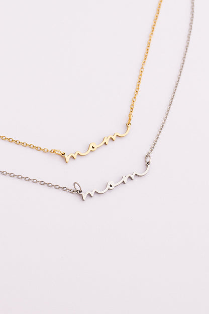 Two gold necklaces with 'mom' and 'mommy' inscriptions on a light pink background
